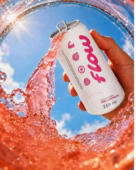 Lata de Flow Pink Lemonade na mão, com splash rosa e céu azul ao fundo